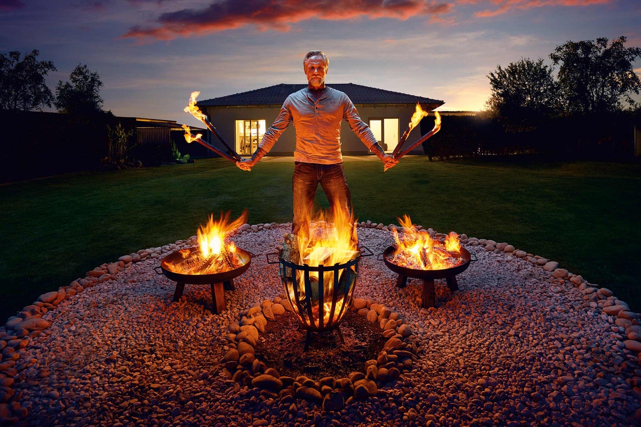 Man med facklor och eldfat i trädgården i skymningen
