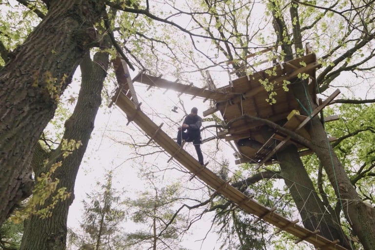 Trädkoja med hängbro och en person på bron.