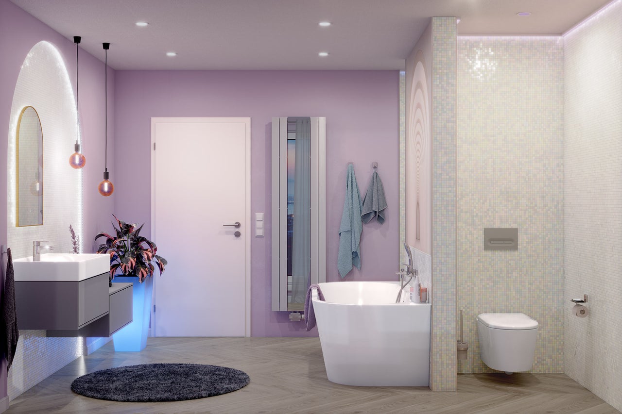 Modernt badrum med lavendelfärgade väggar, fristående badkar, vägghängd toalett, grå kommod och golv i träoptik.
