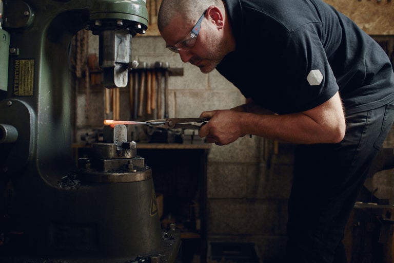 En smed bearbetar glödande metall med en smidesmaskin.