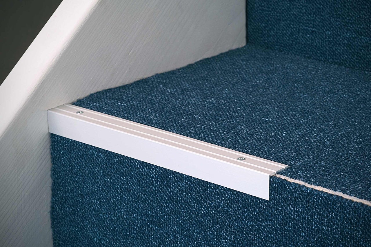 Detaljbild av trappsteg med blå matta och trappkantsprofil av metall