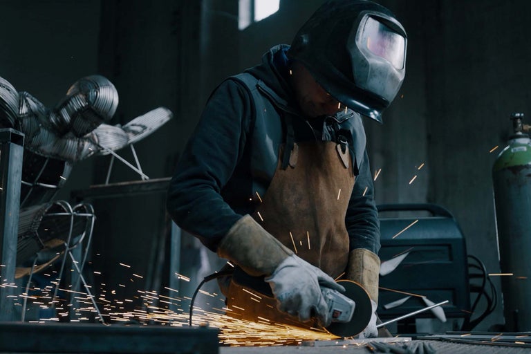 Man med skyddshjälm och förkläde använder vinkelslip i verkstad