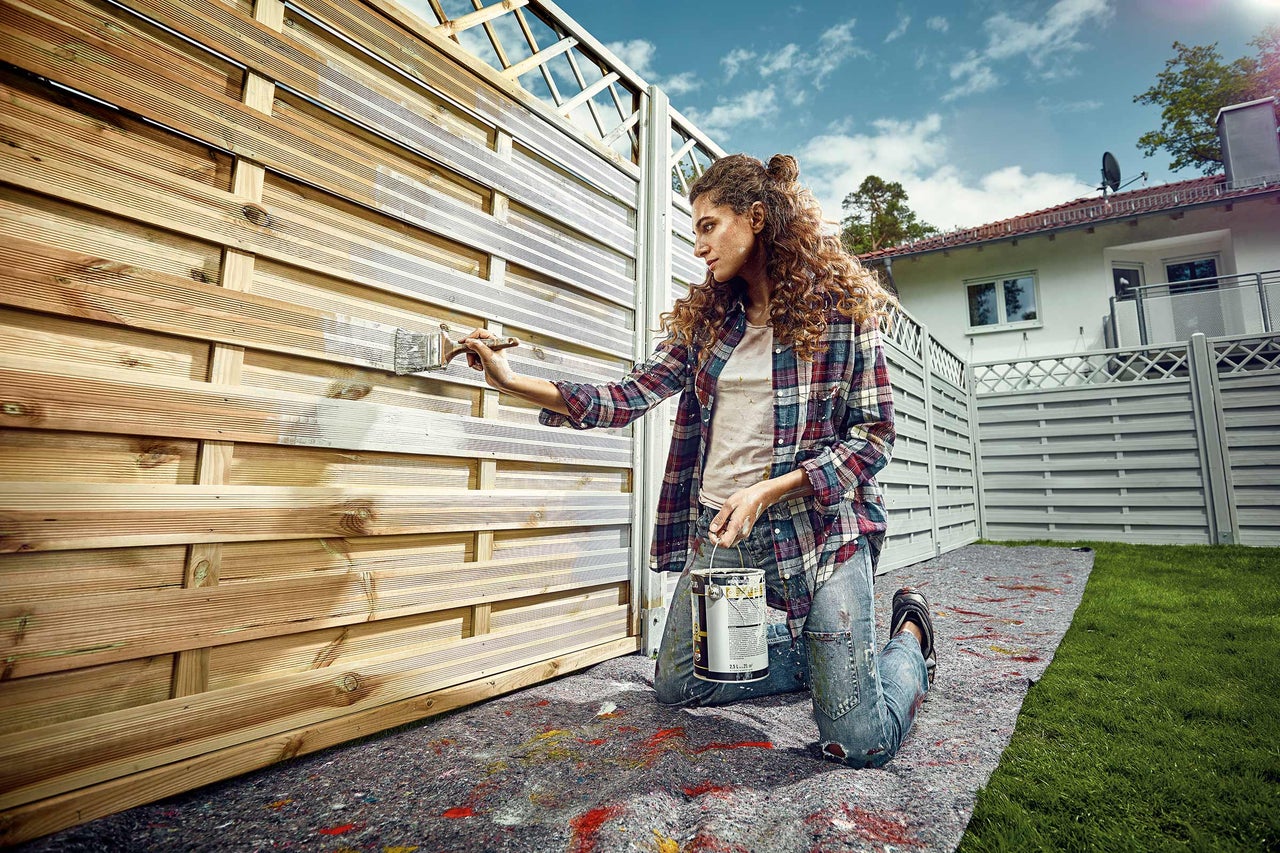 En kvinna målar ett trästaket med en lasyr.