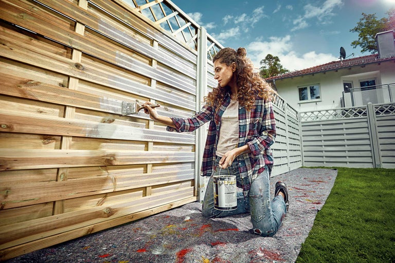 En kvinna målar ett trästaket med en lasyr.