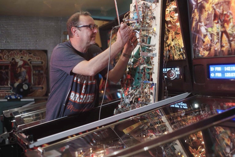 En man reparerar en flipperspel.