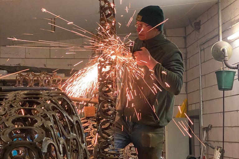 En man bearbetar ett metallobjekt med en vinkelslip, gnistor sprutar.