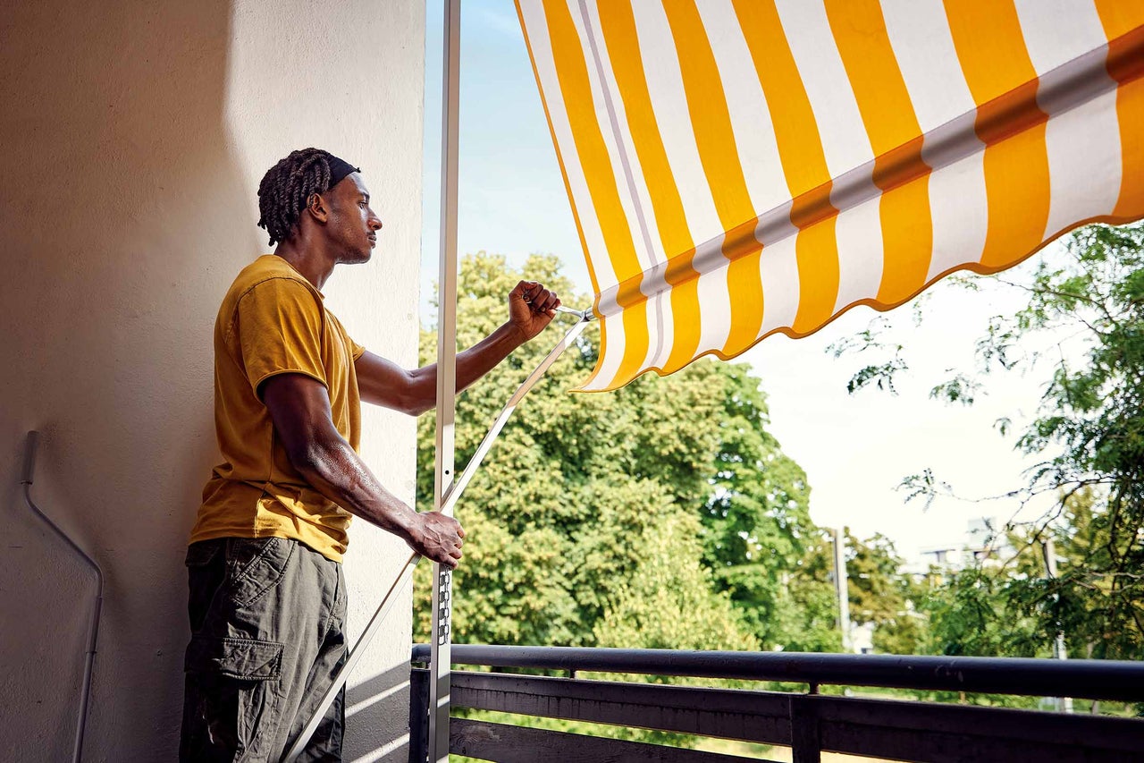 Man som använder en gulrandig markis på en balkong.