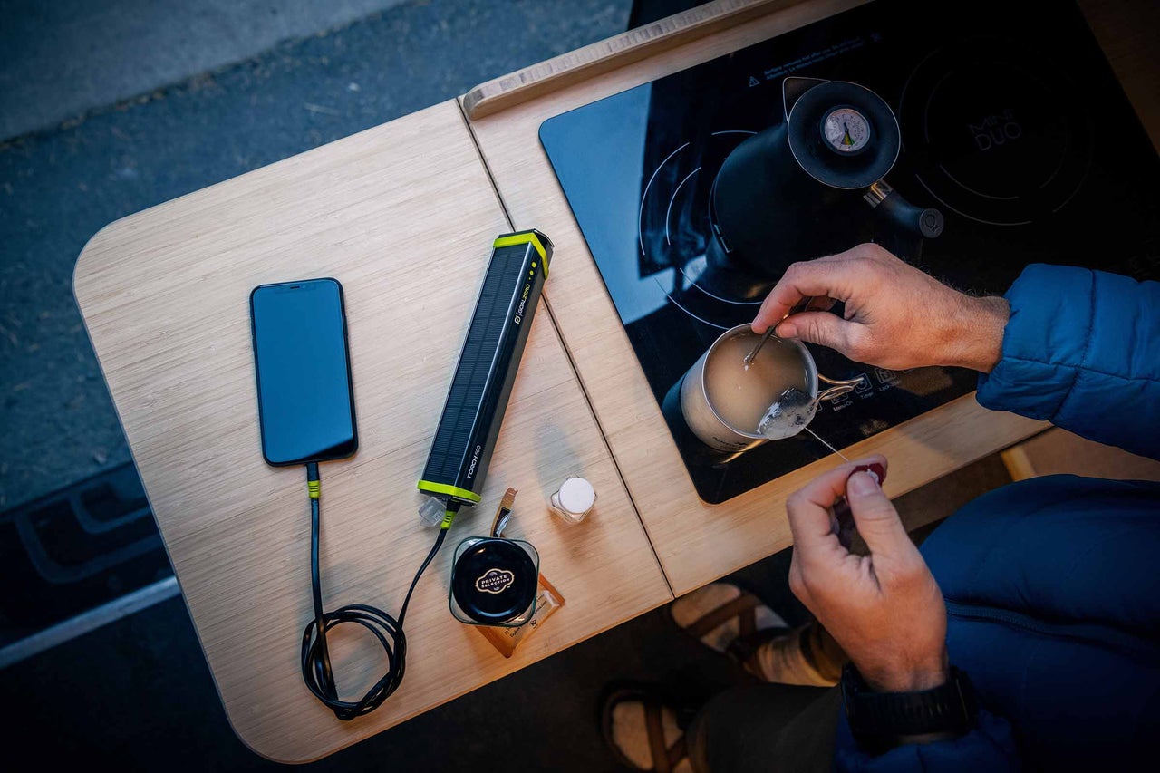 Scen med smartphone, Goal Zero Torch 500 solcellsladdare, kokplatta, tekanna och person som gör te