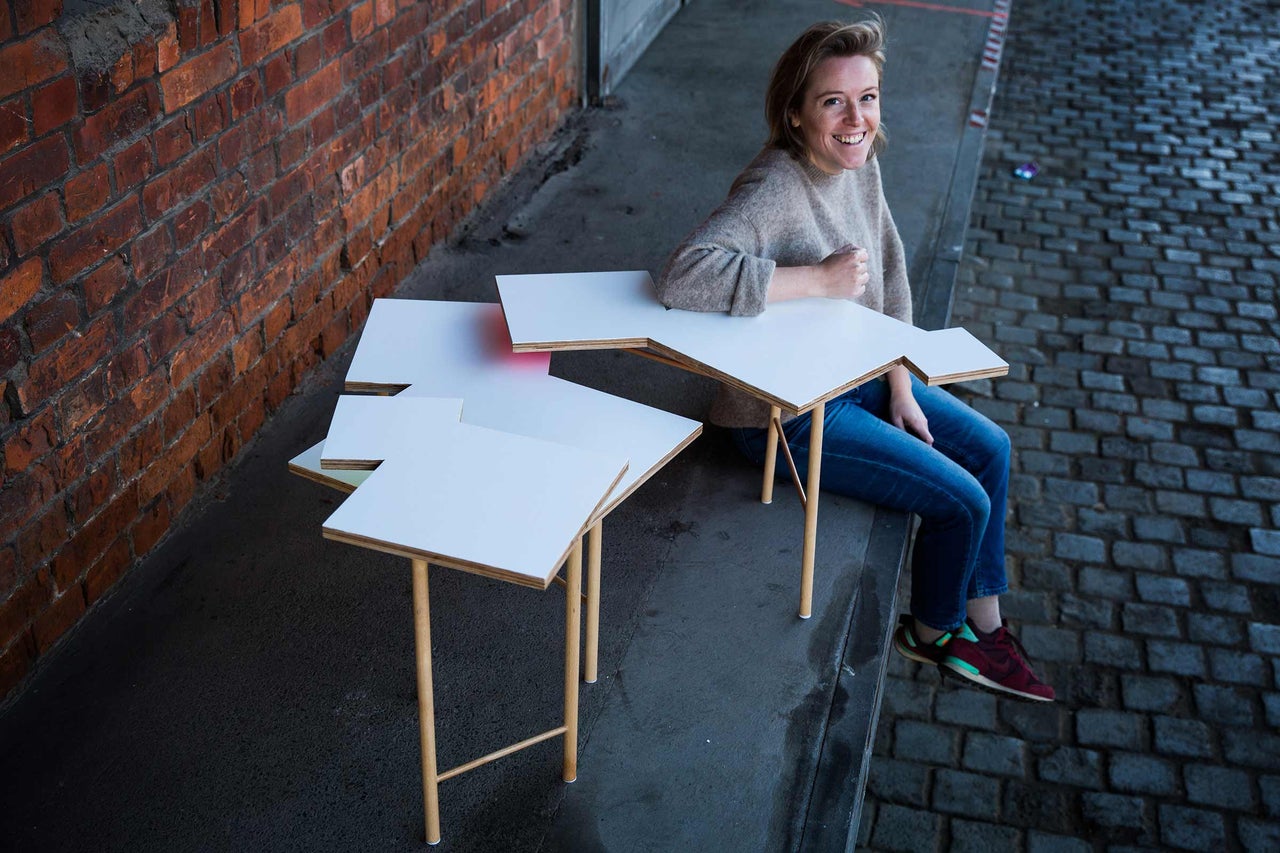 Kvinna sitter bredvid ett bordssystem av trä och vitt för inomhusbruk framför en tegelvägg.