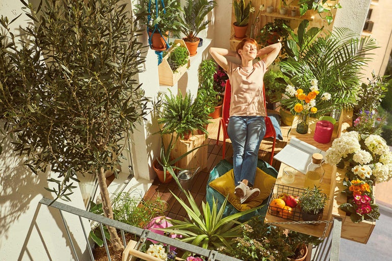 Kvinna kopplar av på en grönskande balkong med växter i krukor och blomlådor.