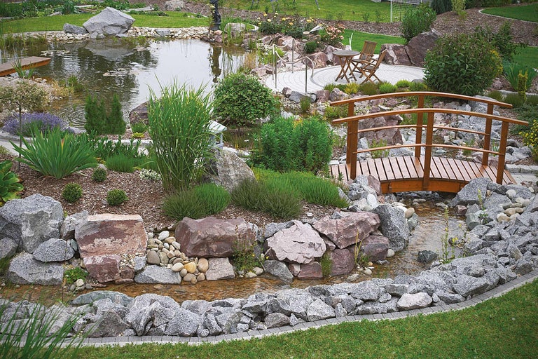 Trädgårdsdamm med träbro, stenar och plantering