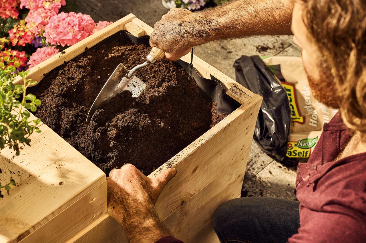 Person fyller en upphöjd rabatt med planteringsjord och en liten spade.