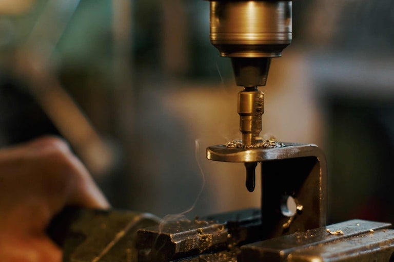 Metallborr borrar genom ett metallstycke i ett skruvstäd.