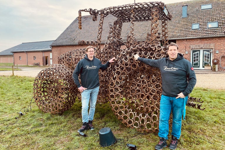 Skulptur av en traktor gjord av hästskor med två personer