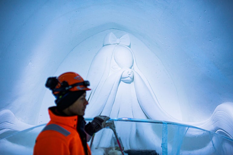 Isskulptur av en hund med rosett, gjord av en arbetare med hjälm och varselväst.