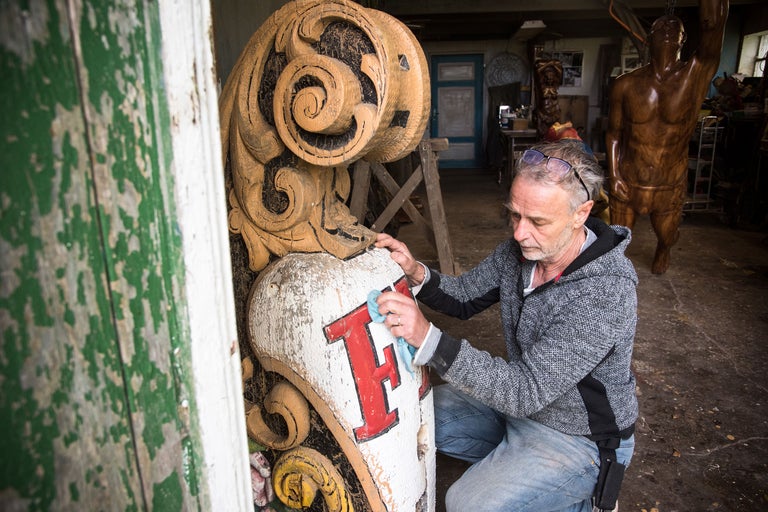 En man rengör en dekorativ träskulptur i en verkstad.