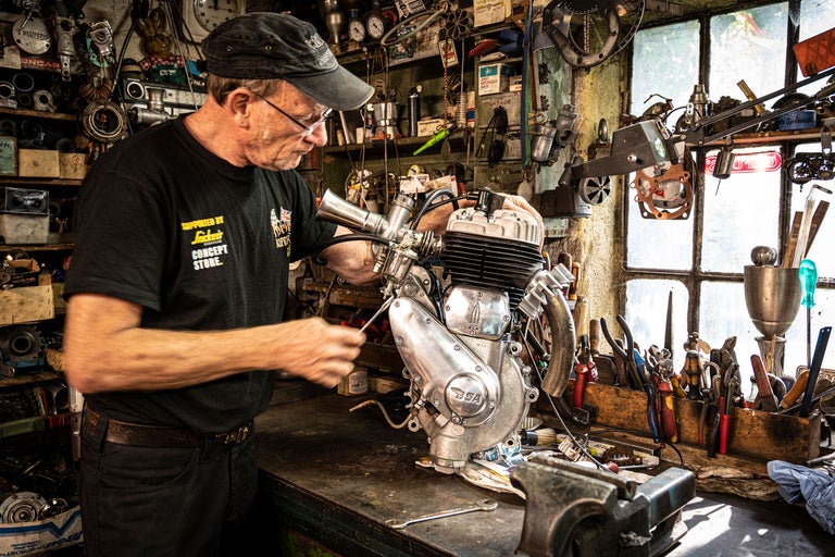 Man arbetar på motorcykelmotor i verkstad med verktyg.