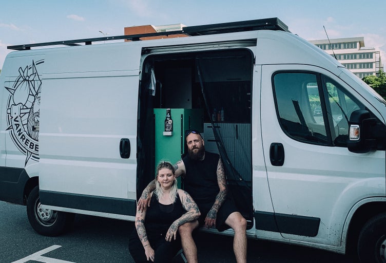 Ett par sitter framför en skåpbil med öppen dörr. Det finns en logotyp på sidan av fordonet.