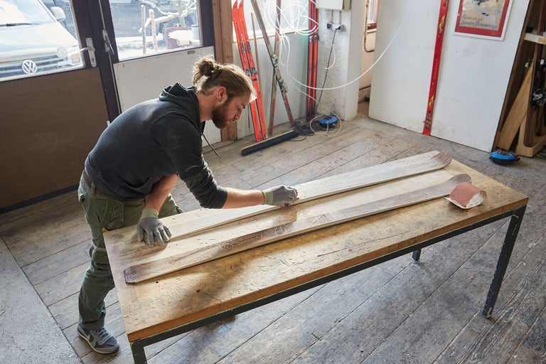 Man slipar träskidor på en arbetsbänk i en verkstad