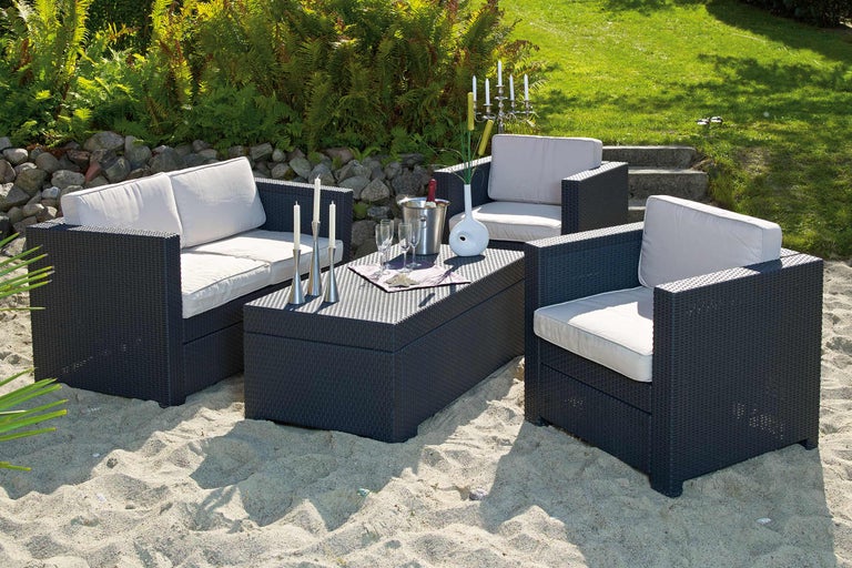 Trädgårdsmöbelset med två fåtöljer, en soffa och ett bord på en sandyta