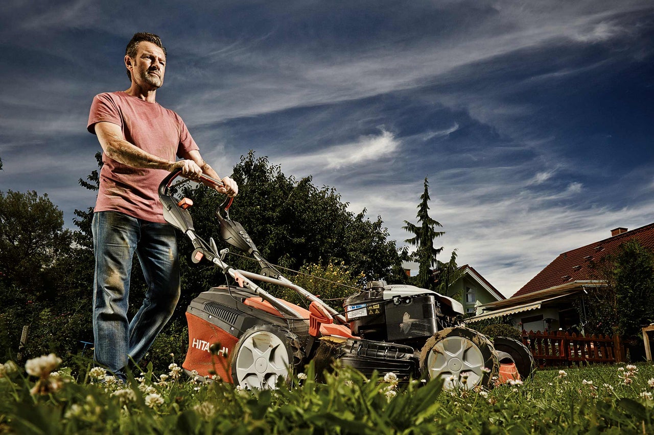 Man klipper gräs med en gräsklippare i trädgården.