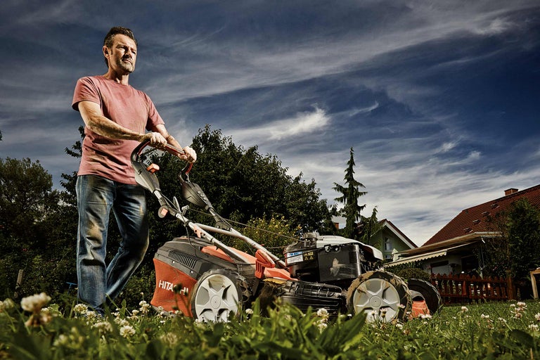 Man klipper gräs med en gräsklippare i trädgården.