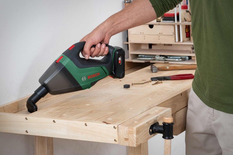 En man rengör en arbetsbänk med en batteridriven handdammsugare från Bosch