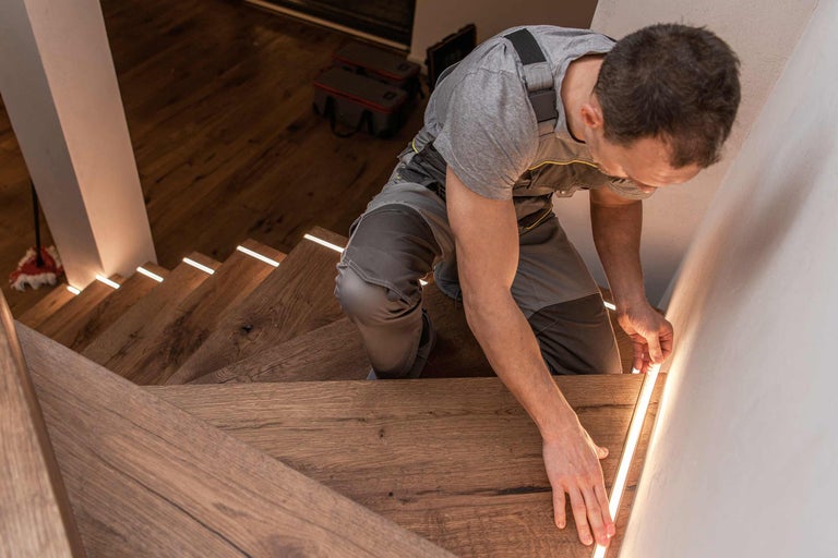 Hantverkare installerar LED-belysning på trätrappa för Hornbach