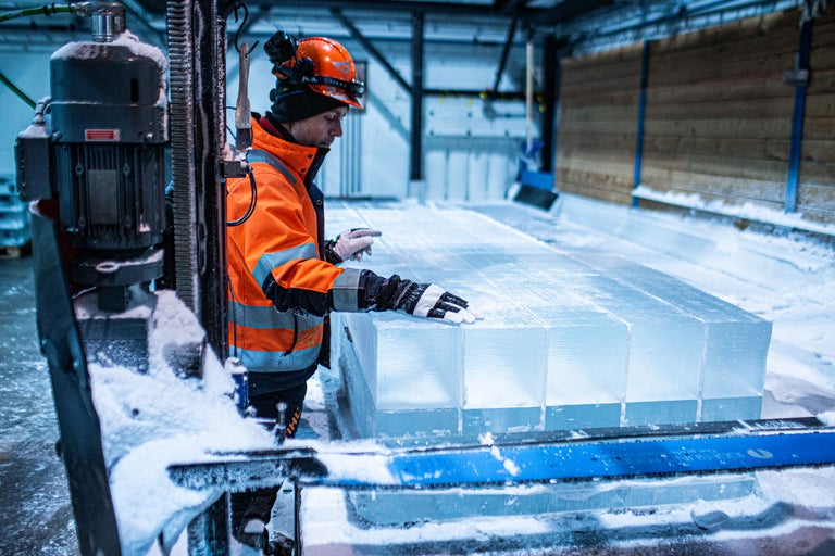 En arbetare med skyddshjälm och varselväst står bredvid isblock.