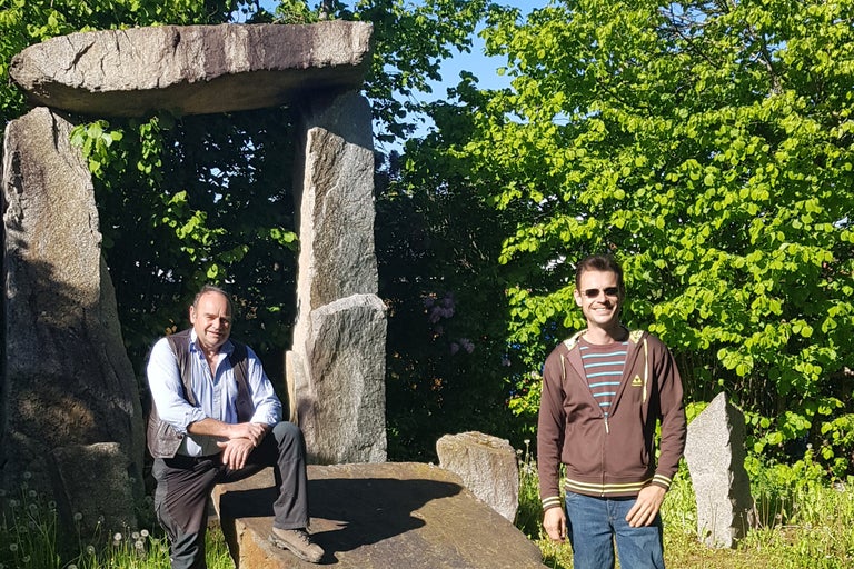 Två män framför en stenbåge i en trädgård.