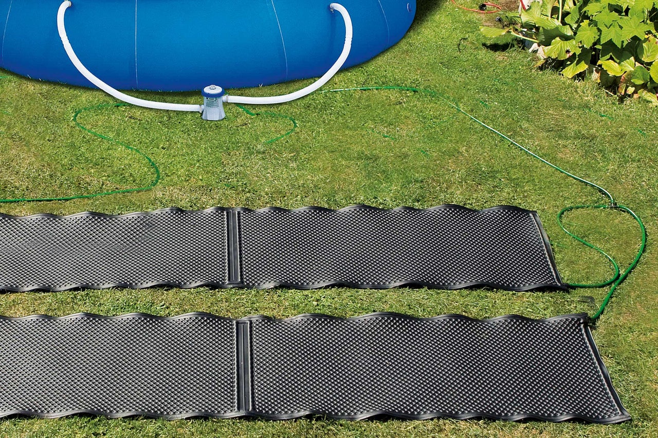 Två soluppvärmningsmattor på en gräsmatta nära en pool med filterpump.