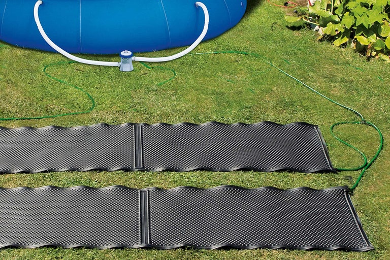 Två soluppvärmningsmattor på en gräsmatta nära en pool med filterpump.