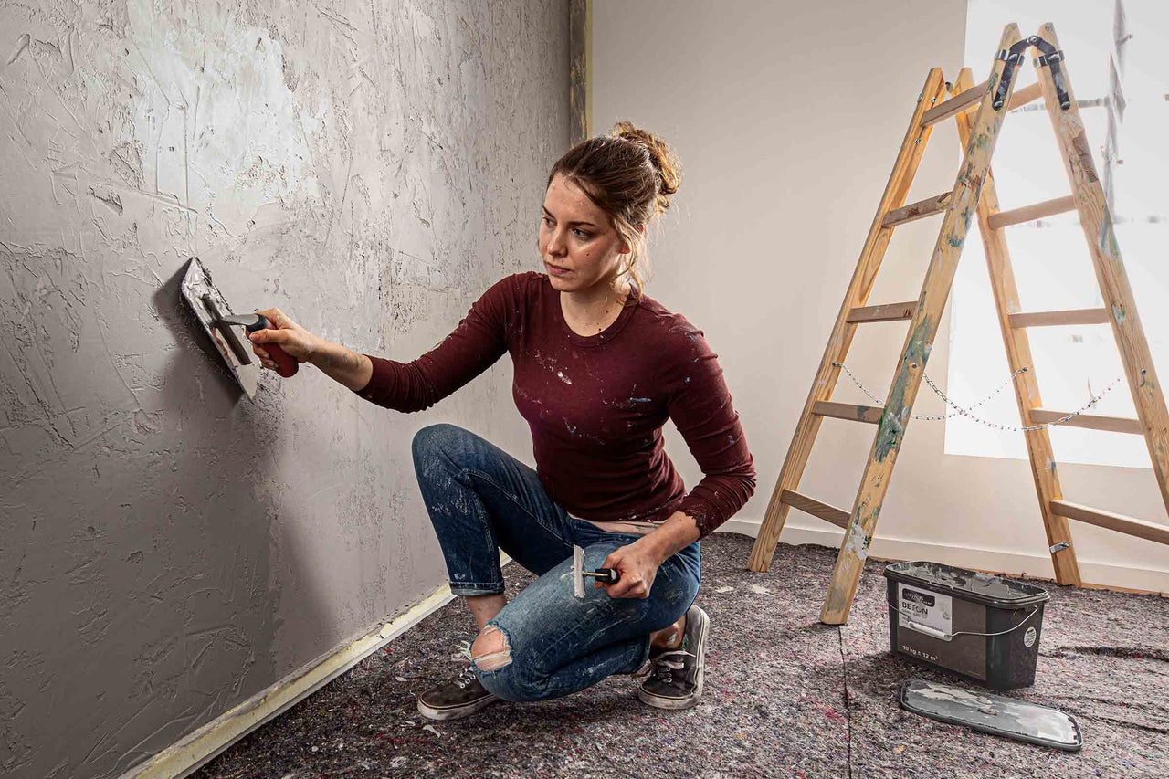Kvinna applicerar betongspackel på en vägg med en spackelspade, bredvid en stege.