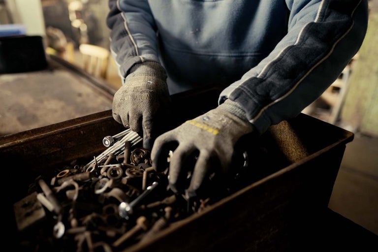 En person söker igenom en låda med skruvar och muttrar med arbetshandskar.