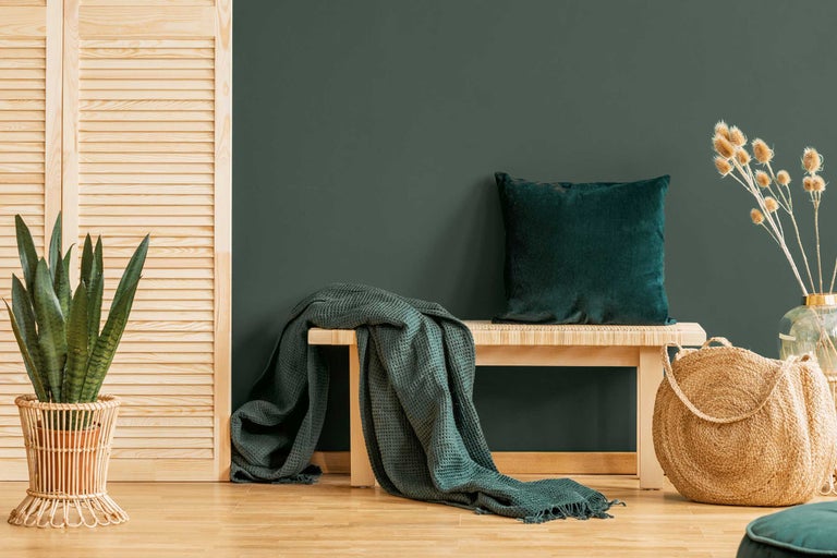 Dekorativ boendemiljö med bänk, kudde, filt, växt och flätad korg
