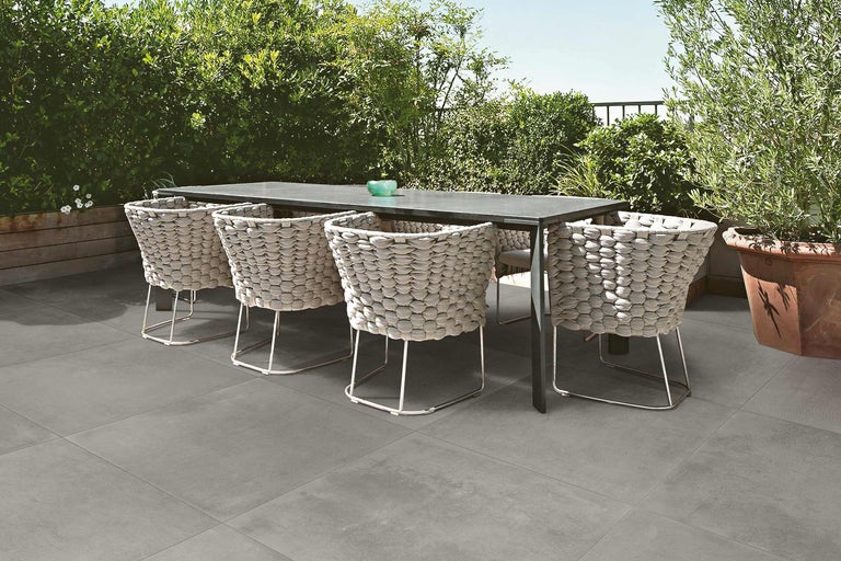 Matbord med korgstolar på grå uteplatsplattor i trädgården