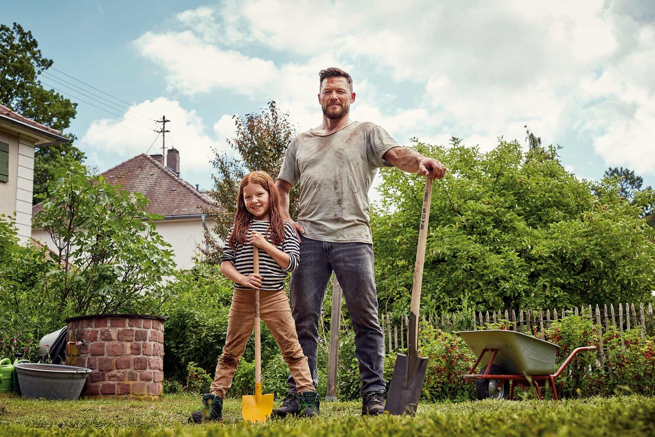 Far och dotter i trädgården med spade och skottkärra