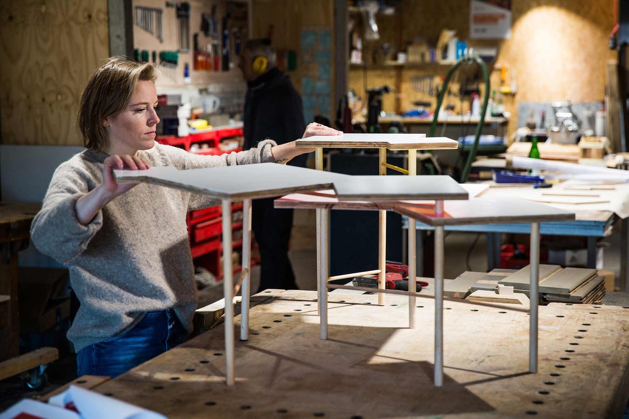 Kvinna i verkstad arrangerar träkonstruktion med bordsskivor och ben
