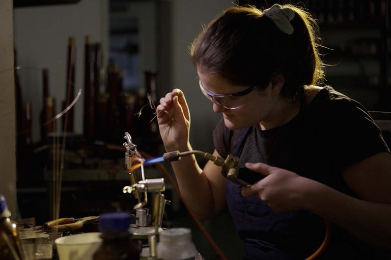 Kvinna med skyddsglasögon och lödlampa som bearbetar glas.