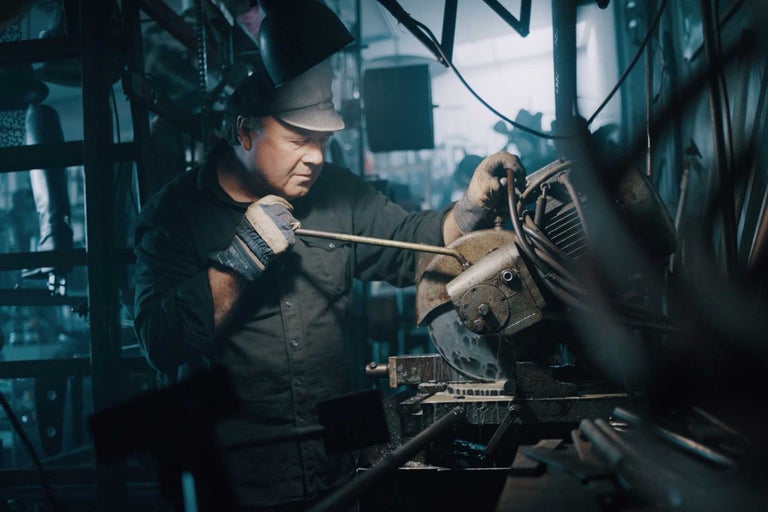 En man skär en bit metall med en metallsåg medan han bär skyddskläder.