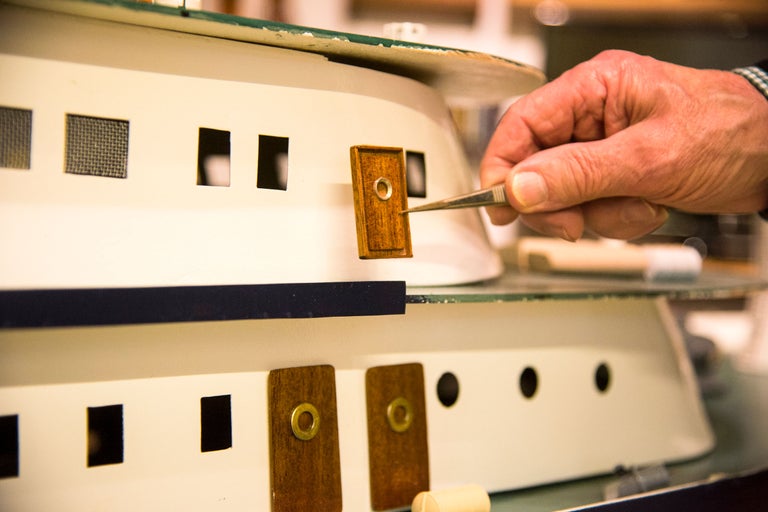 Närbild av en fartygsmodell med pincett som håller en liten träbit