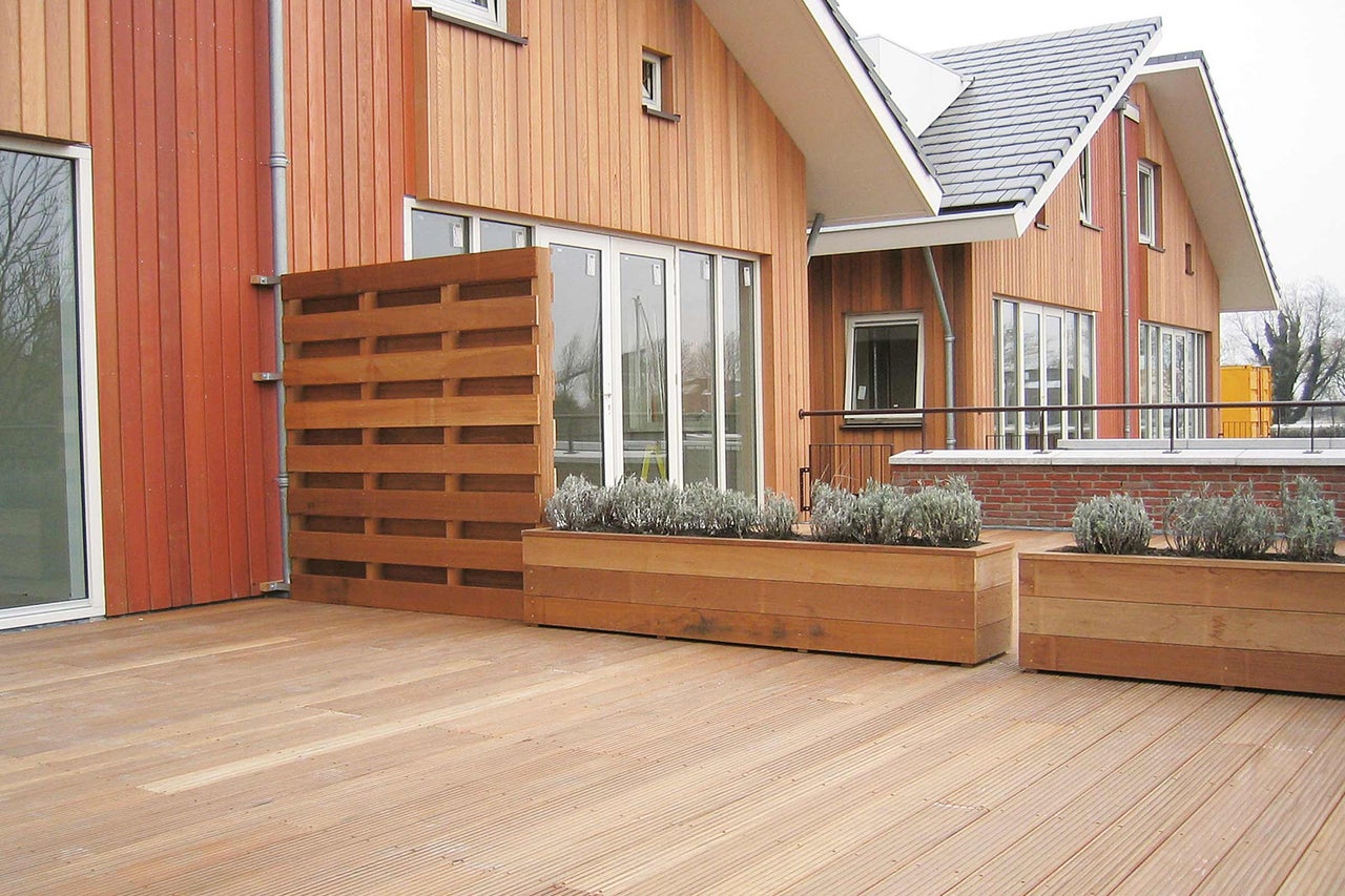 Trädäck med insynsskydd och planterade blomlådor framför ett hus