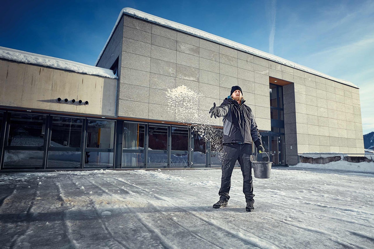Man strör salt på en isig yta framför en byggnad