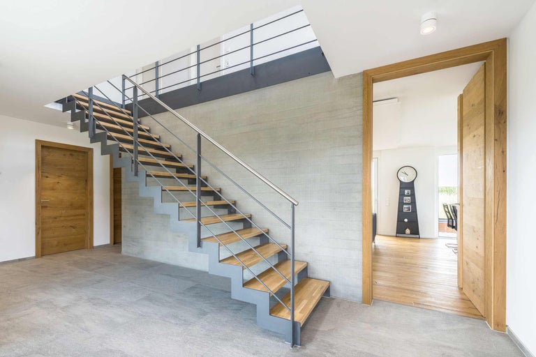 Interiör av ett modernt hus med trappa, trädörrar och klinkergolv.