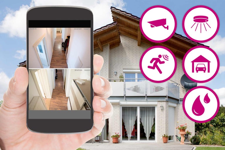 En smarttelefon i handen visar ett husövervakningssystem med olika säkerhetssymboler framför ett hus.