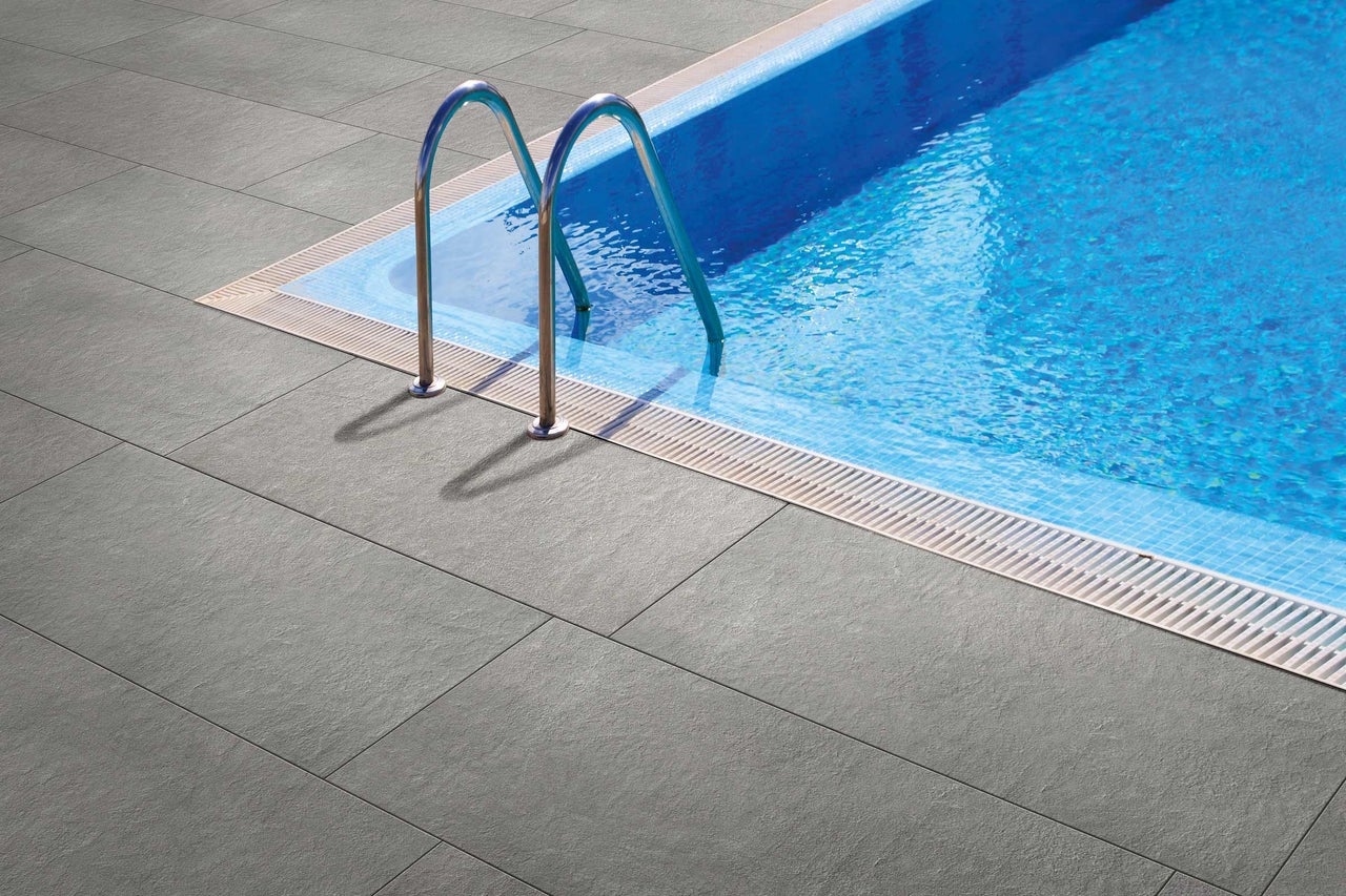 Grå terrassplattor bredvid en pool med stege.