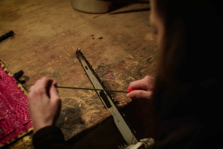 En person skärper en motorsåg med ett skärpverktyg på en arbetsbänk.