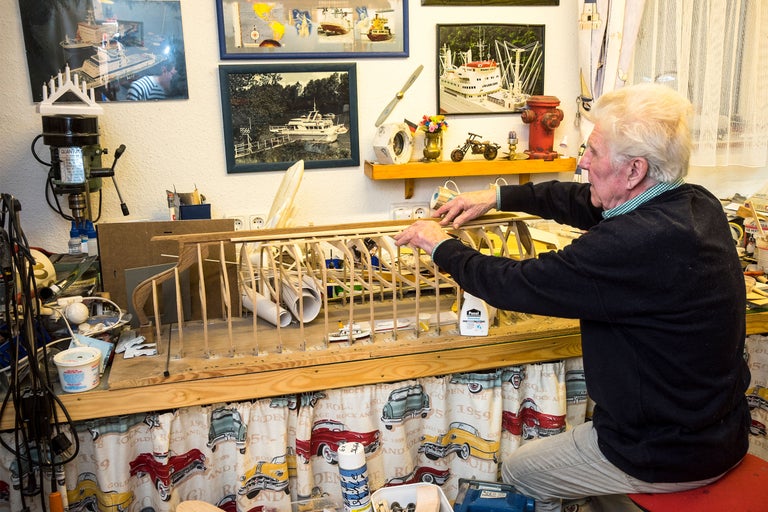 Man bygger ett modellflygplan i trä i sin verkstad med verktyg och bilder på väggen