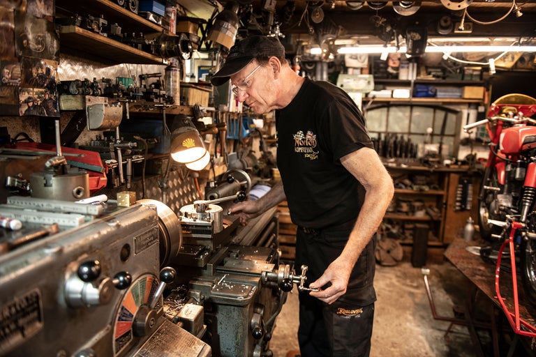 Man arbetar vid en svarv i en verkstad med en motorcykel