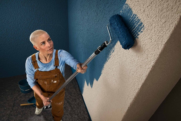En person målar en vägg med en färgroller.